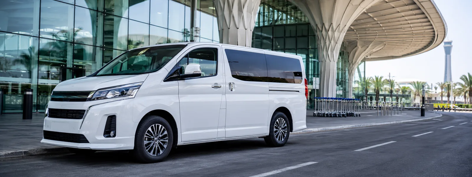 White airport transfer van outside a modern Dubai terminal